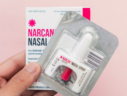 Hand holding a package of Narcan on a pink background.